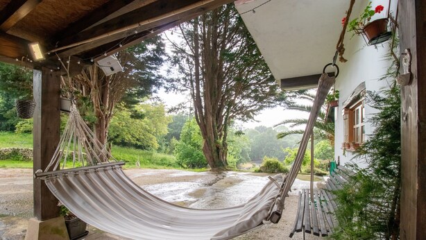 Una hamaca colgada bajo una estructura de madera, con vista a un jardín y un edificio al fondo.