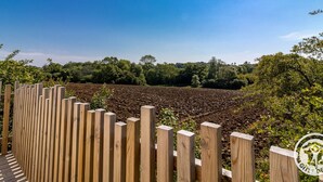 Een houten hek met uitzicht op een bewerkt veld en bomen op de achtergrond.
