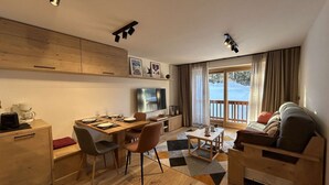 A modern living room with a dining area, wooden flooring, a flat-screen TV, and a view of the outdoors. - Renovated apartment in Méribel, near slopes, fiber included (Méribel)