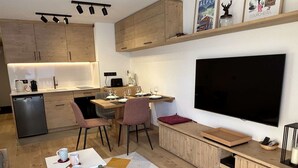 A modern kitchen with a dining area, a large flat-screen TV, and a small seating area with a rug. - Renovated apartment in Méribel, near slopes, fiber included (Méribel)