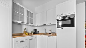 Una cocina moderna con armarios blancos, encimera de madera, horno empotrado y cafetera.