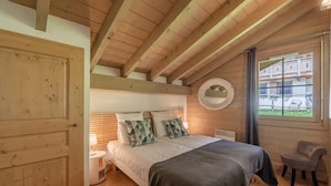 Ein Schlafzimmer mit Holzboden, einem Bett, einem runden Spiegel und einem Fenster mit Blick auf ein Gebäude.