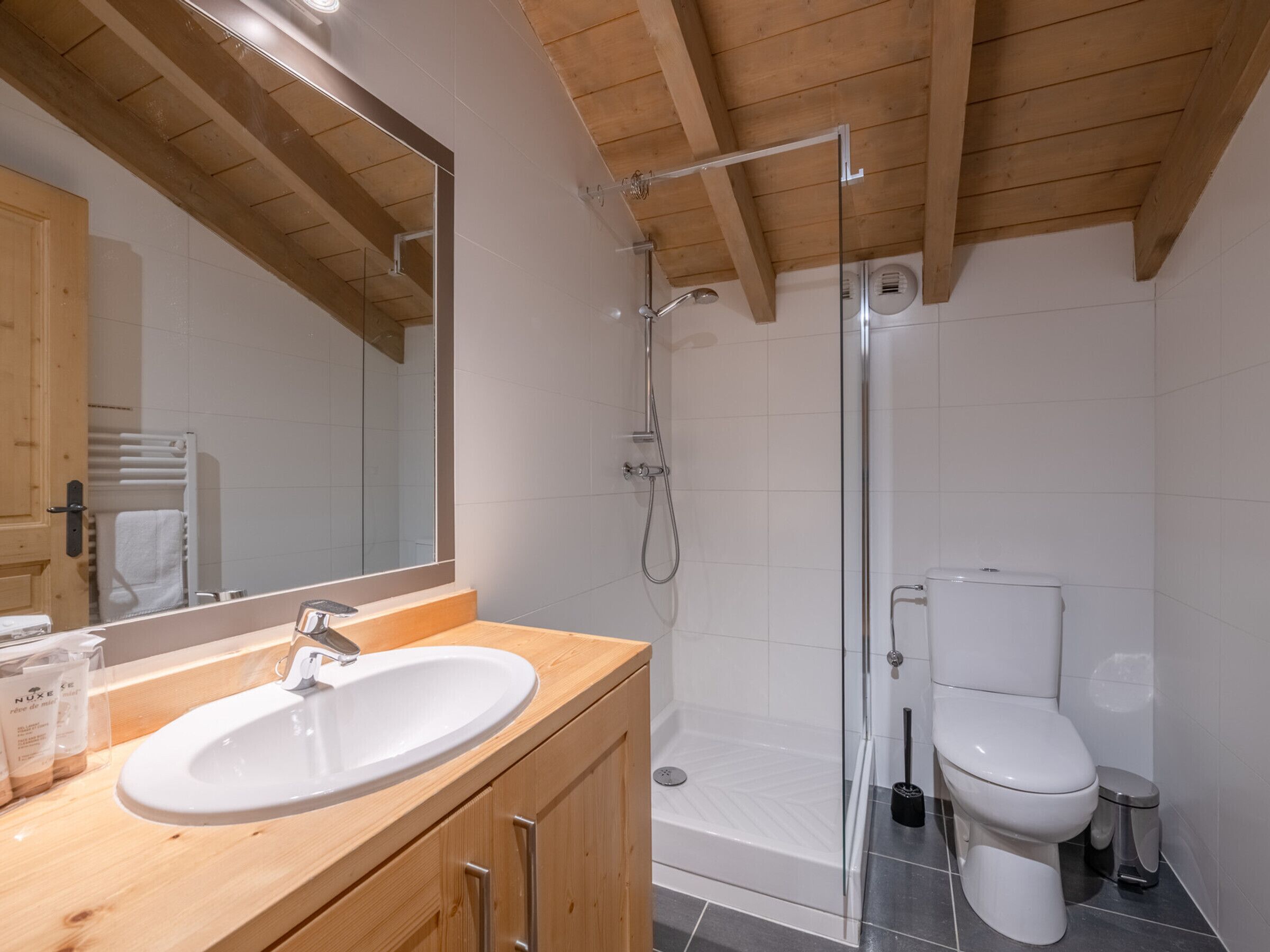 Une salle de bain moderne avec un meuble-lavabo en bois, une cabine de douche en verre et des toilettes blanches.