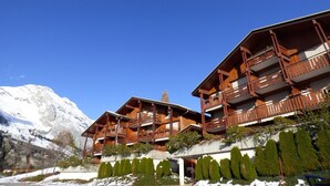 A wooden chalet with multiple balconies, set against a mountainous backdrop. - Charming ski-in T3, 6 pax, balcony, garage (Le Grand-Bornand)