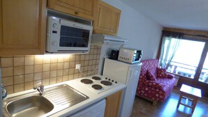 A compact kitchen with a microwave, a toaster, and a sink. There is a small refrigerator and a dining area with a table and chairs. - Charming ski-in T3, 6 pax, balcony, garage (Le Grand-Bornand)