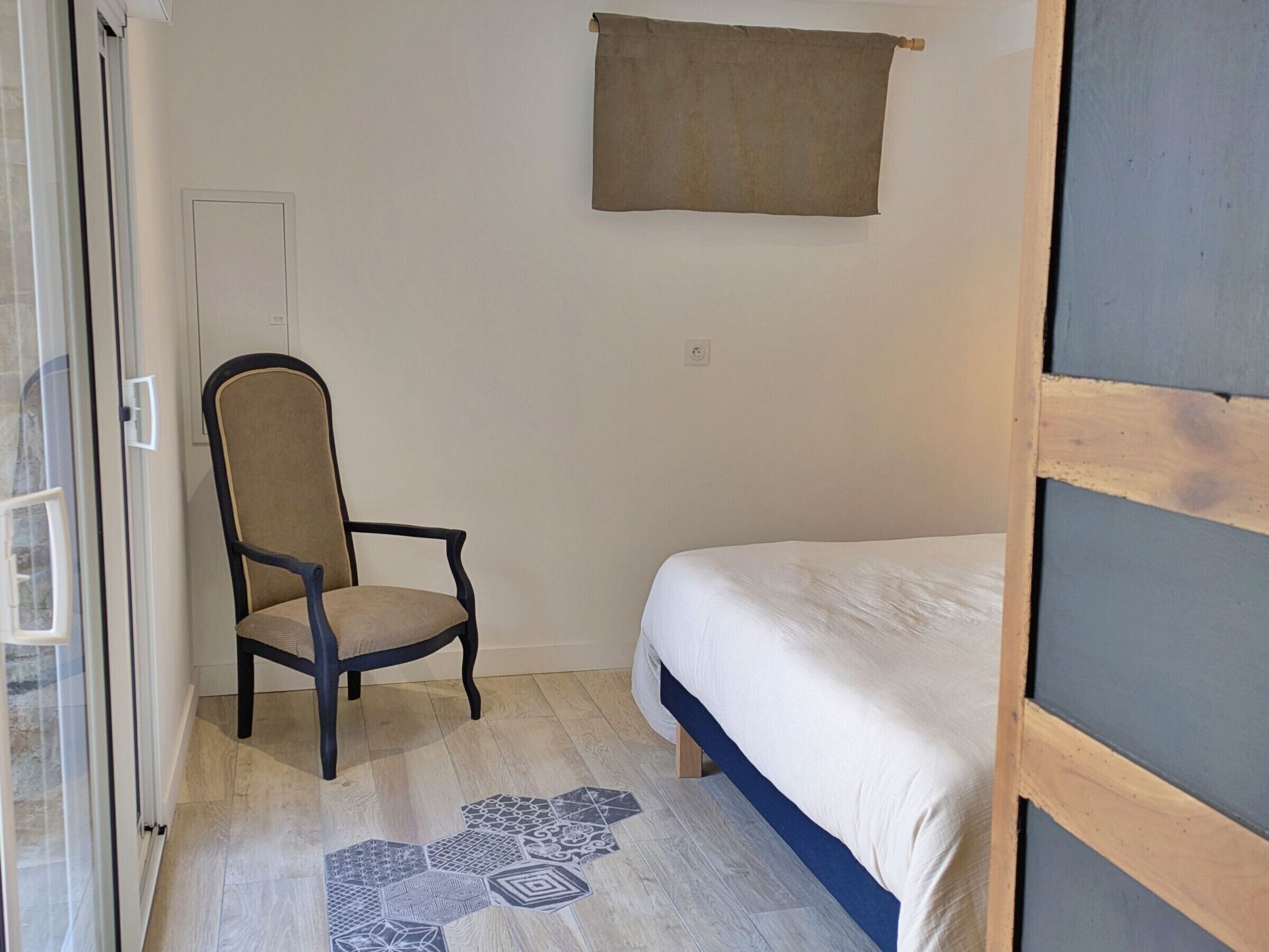 Een kleine kamer met een bed, een stoel en een raam.