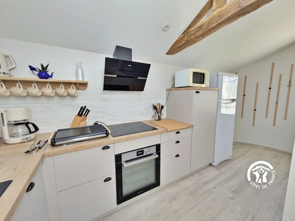 A modern kitchen with a built-in oven, microwave, and coffee maker. There are wooden shelves with cups and a blue vase.
