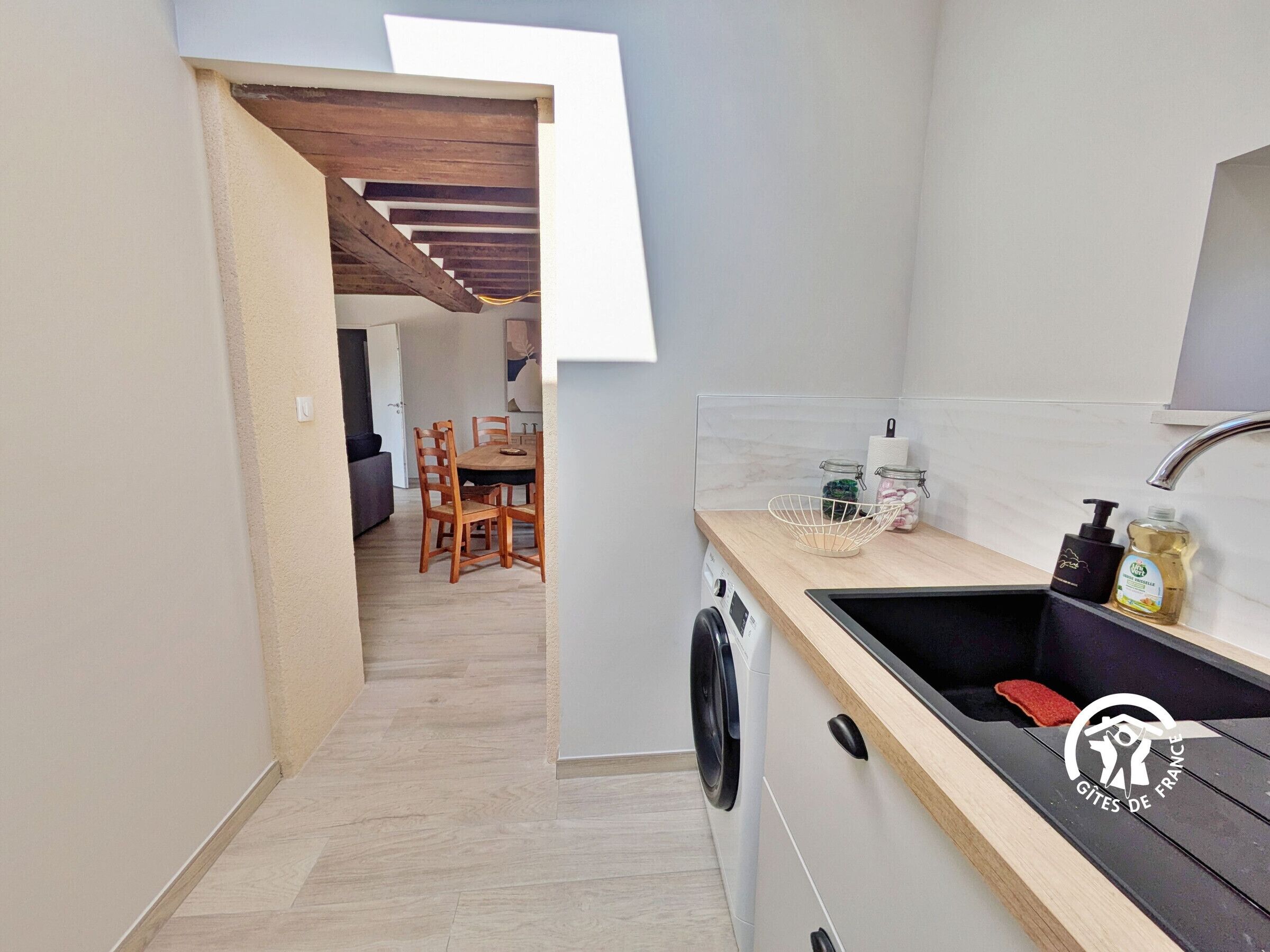 Een kleine keuken met een wasmachine, een spoelbak en een eethoek met stoelen.
