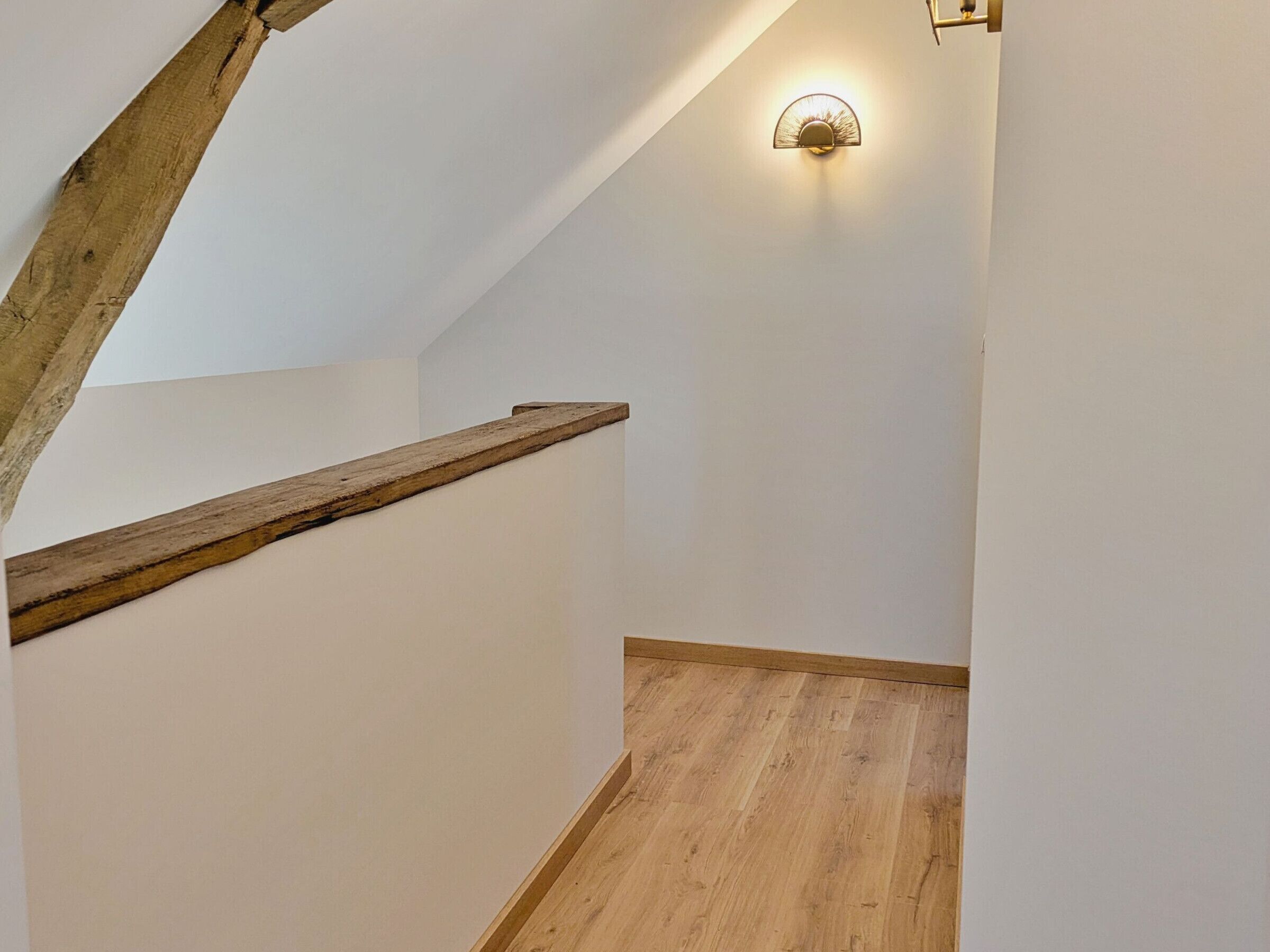 A wooden staircase with a handrail, white walls, and a wall-mounted light fixture.