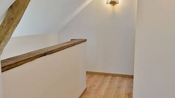 A wooden staircase with a handrail, white walls, and a wall-mounted light fixture.