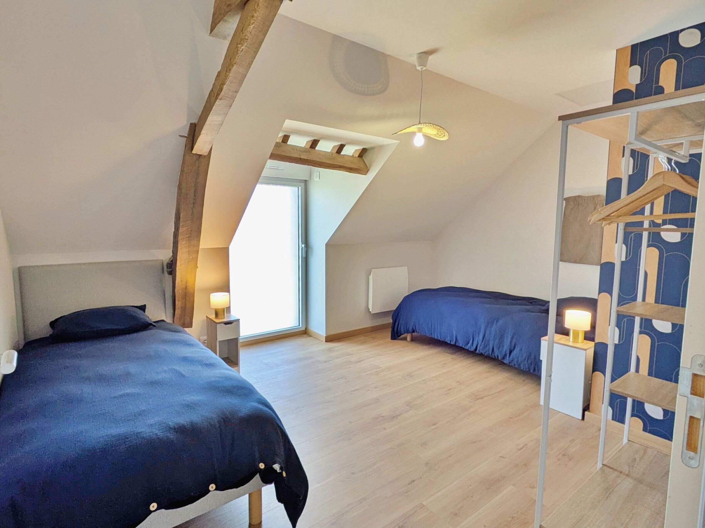 A bedroom with two beds, a wooden ceiling, a skylight, and a wardrobe with a geometric pattern.