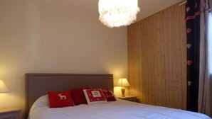 A bedroom with a bed, two bedside lamps, a wooden headboard, and a hanging light fixture. - Charming 4-room + mezzanine for 8 people in Grand-Bornand (Le Grand-Bornand)
