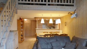 A cozy living room with a grey sofa, wooden staircase, and a kitchen in the background. - Charming 4-room + mezzanine for 8 people in Grand-Bornand (Le Grand-Bornand)