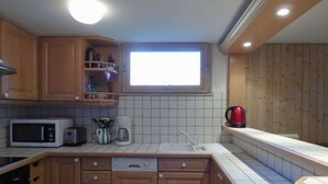 A compact kitchen with wooden cabinets, a microwave, a toaster, a kettle, and a window above the sink. - Charming 4-room + mezzanine for 8 people in Grand-Bornand (Le Grand-Bornand)