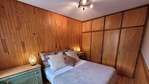 A bedroom with a wooden wardrobe, a bed with patterned bedding, and bedside lamps.