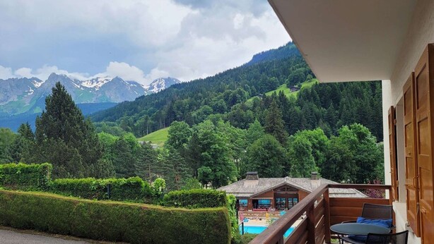 A balcony with a view of a mountain landscape, a pool, and a wooden building.