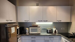 A kitchen with white cabinets, a stainless steel refrigerator, a microwave, a toaster, and a coffee maker.
