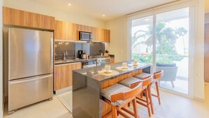 A modern kitchen with a central island, stainless steel appliances, and a view to a balcony. - Chic Beachfront Condo Ocean View (Akumal)