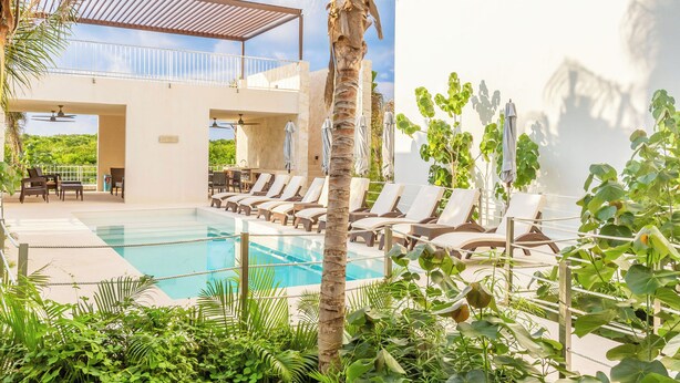 A pool area with lounge chairs and a covered seating area. - Chic Beachfront Condo Ocean View (Akumal)