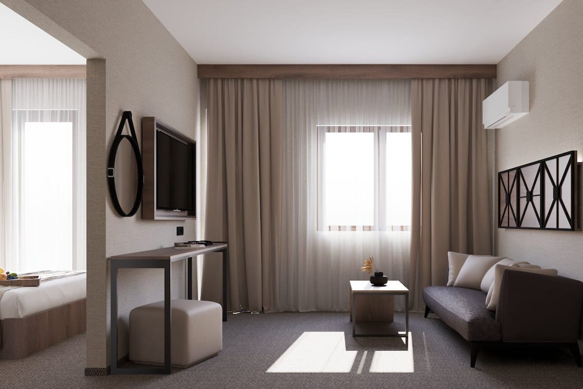A modern hotel room with a bed, a desk, a sofa, and a TV.