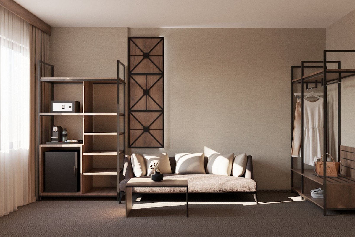 A modern hotel room with a sofa, a small table, a wardrobe, and a built-in shelving unit.