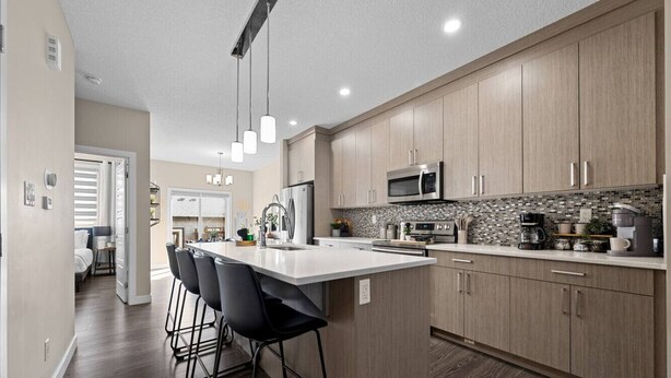 A modern kitchen with a central island, bar stools, stainless steel appliances, and a backsplash. - 6 BR | Sleep 12 | Stadium & Rogers | Yard | Garage (Edmonton)