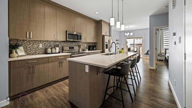 A modern kitchen with wooden cabinets, a central island with bar stools, stainless steel appliances, and pendant lighting. - Modern 4BR | Yard | Garage | Near Stadium & Rogers (Edmonton)