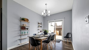 A dining area with a table set for four, surrounded by black chairs, a chandelier, and shelves with various items. - Modern 4BR | Yard | Garage | Near Stadium & Rogers (Edmonton)