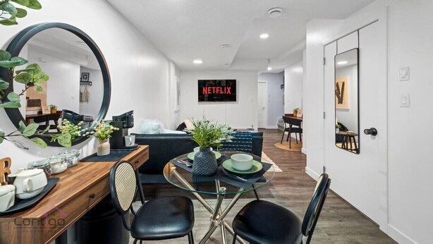 A modern living room with a round glass table, black chairs, a sofa, and a large mirror. A TV screen displays the Netflix logo. - Cozy 2BR Bsmt Suite | Near Commonwealth & Rogers! (Edmonton)