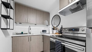 A modern kitchen with stainless steel appliances, wooden cabinets, and a built-in microwave. - Cozy 2BR Bsmt Suite | Near Commonwealth & Rogers! (Edmonton)
