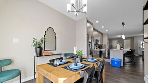 A modern kitchen with stainless steel appliances, a dining area with a wooden table and chairs, and a large mirror on the wall. - 4 BR | Yard | Garage | Near Commonwealth & Rogers! (Edmonton)