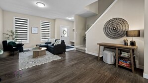 A modern living room with a sectional sofa, a coffee table, and a staircase with a decorative wall piece. - 4 BR | Yard | Garage | Near Commonwealth & Rogers! (Edmonton)