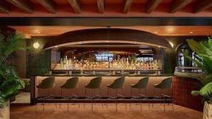 A bar area with a curved wooden ceiling, a variety of liquor bottles, and five modern chairs.