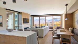 A modern kitchen with a large island, dining area, and a view of mountains.