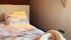 Una cama con almohada con paisaje de montaña, un edredón blanco y mullido, y un cabecero de madera.