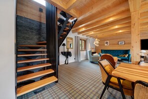 Un interno moderno con una scala in legno, un'area pranzo con pavimento a scacchi e un soggiorno con divano blu.