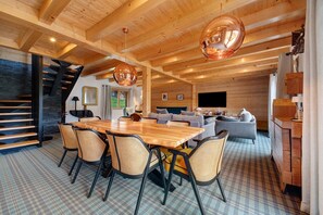 Una habitación amplia con una mesa de comedor de madera, sillas y un sofá. Se ve una escalera con barandilla negra que conduce a un nivel superior.