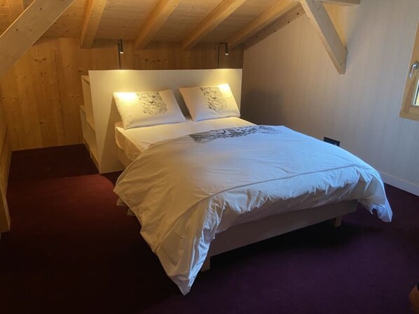 A bedroom with a wooden ceiling, a bed with white bedding, and a purple carpet.