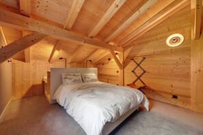 Un dormitorio con techo de madera, una cama con ropa de cama blanca y una mesita de noche.