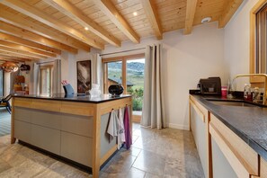 A kitchen with a wooden island, a view of the outdoors, and a dining area with a table and chairs. - Chalet 'Les Carroz De Mary - Sommand' with Mountain View, Private Terrace and Wi-Fi (Mieussy)