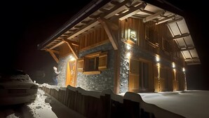 Un camino cubierto de nieve que conduce a una cabaña de madera con fachada de piedra y techo inclinado.