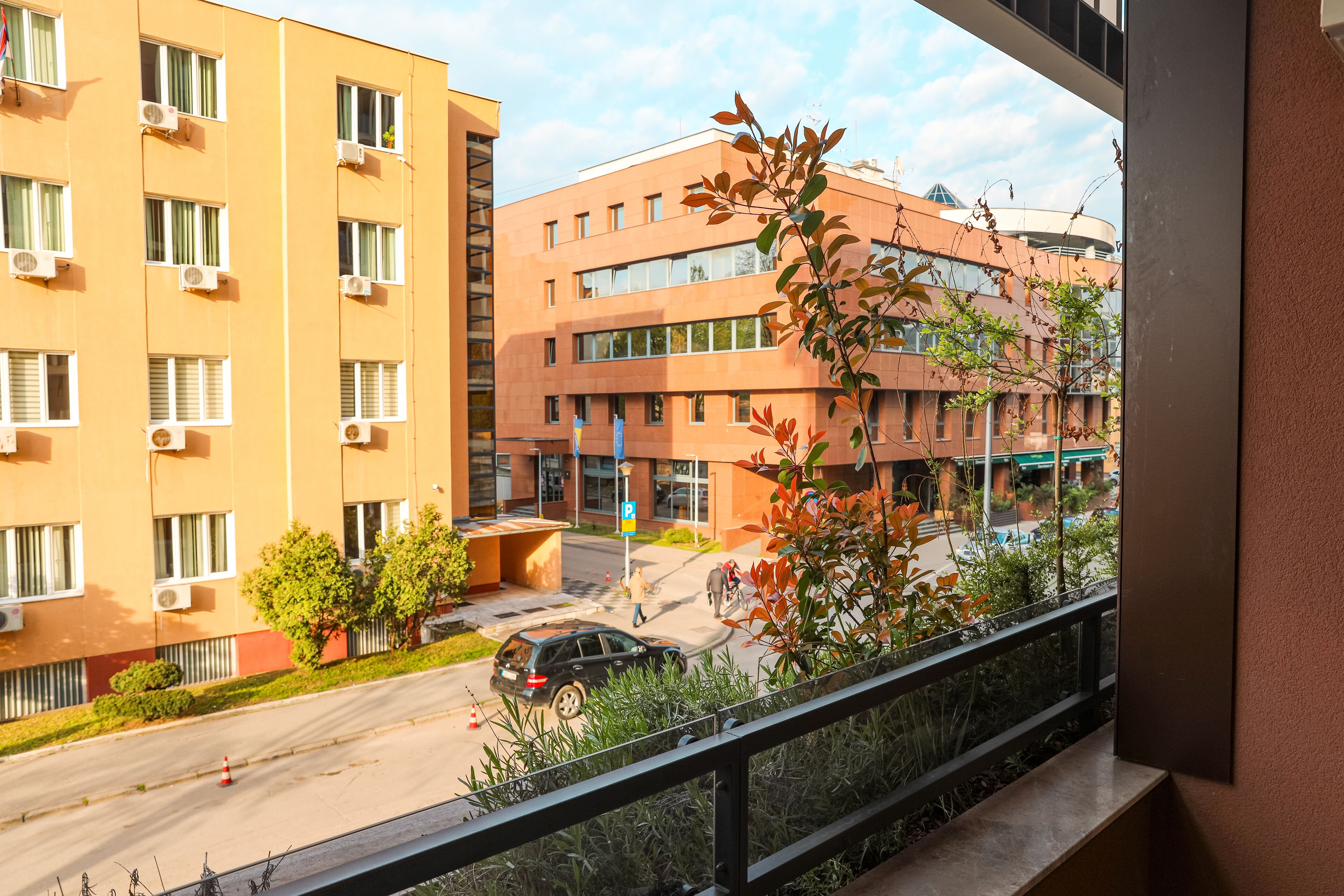A multi-story building with balconies, a parking area, and a clear view of the street.