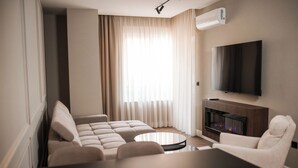 A modern living room with a sofa, armchairs, a coffee table, a flat-screen TV, and a fireplace. - Ideal Apartments (Banja Luka)