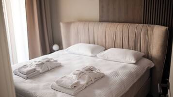A neatly made bed with white linens and towels, a wooden headboard, and a window with curtains.