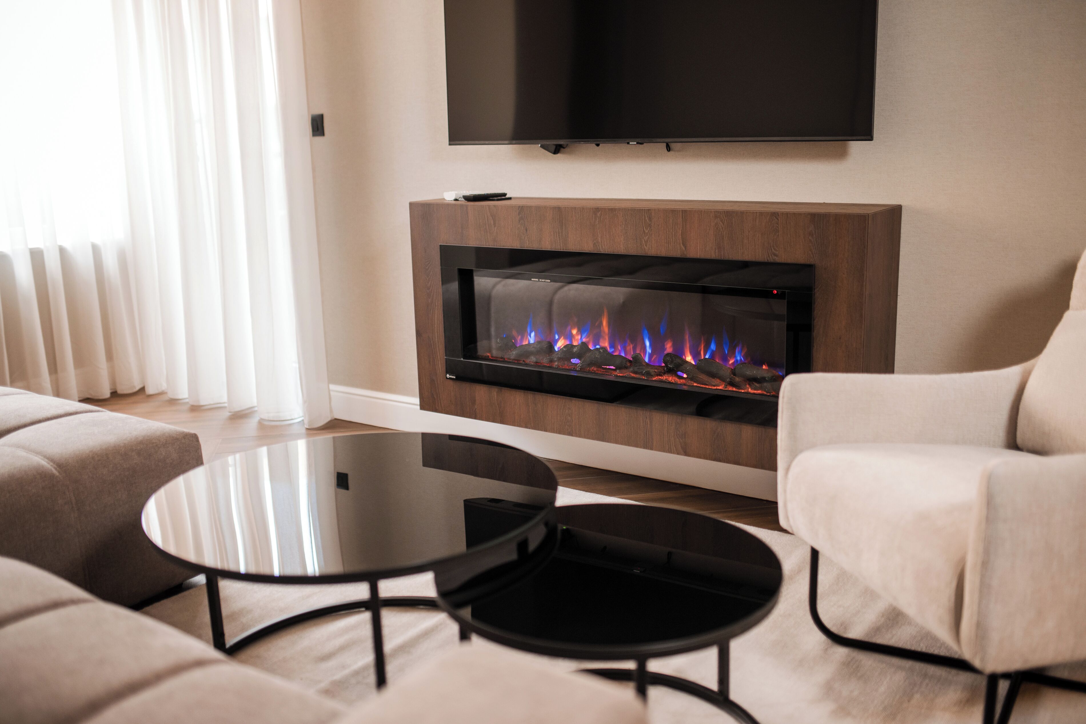 A modern living room with a fireplace, a flat-screen TV mounted on the wall, and a sofa.