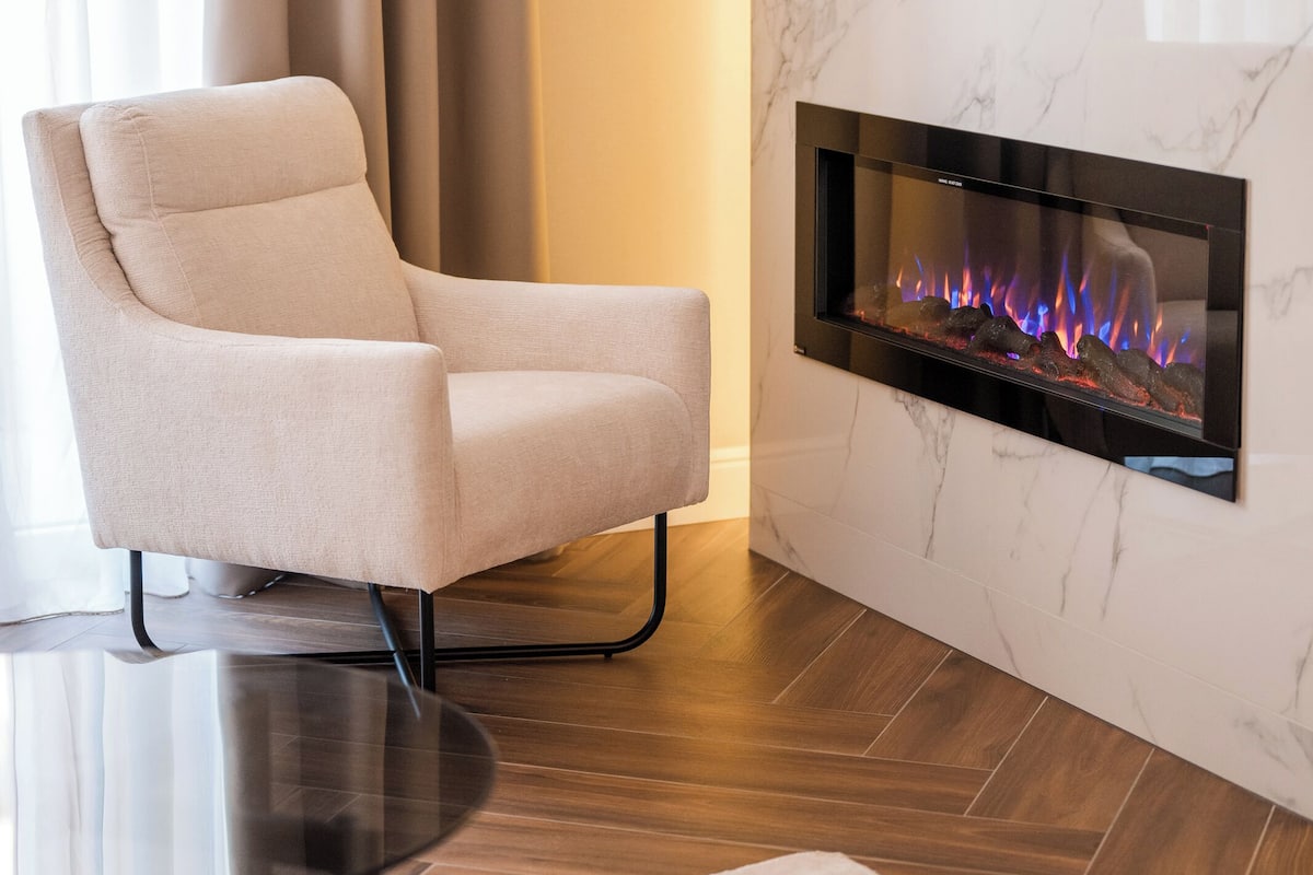 Een moderne woonkamer met een open haard, een comfortabele fauteuil en een ronde glazen tafel.