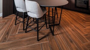 A modern kitchen with a marble backsplash, wooden cabinets, and a dining area with a round table and four chairs. - Ideal Apartments (Banja Luka)