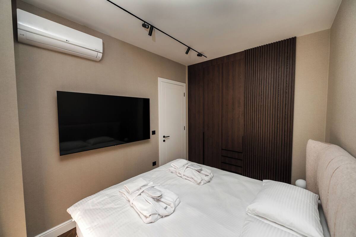 Een hotelkamer met een bed, een flatscreen televisie aan de muur, een houten garderobe en een airconditioner.