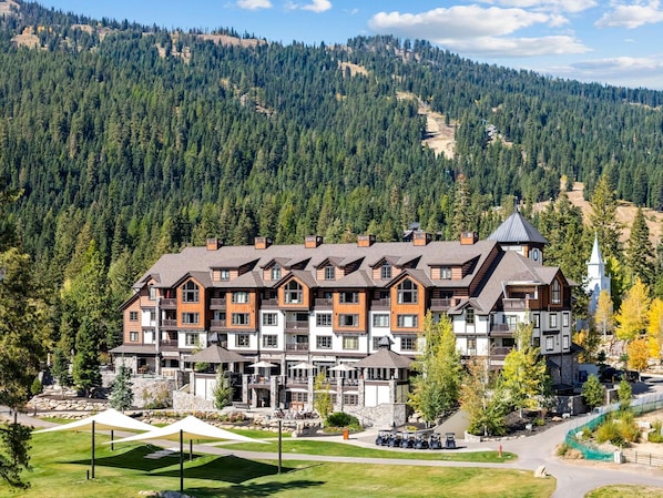 A multi-story hotel with a stone facade, multiple balconies, and a ski resort in the background.