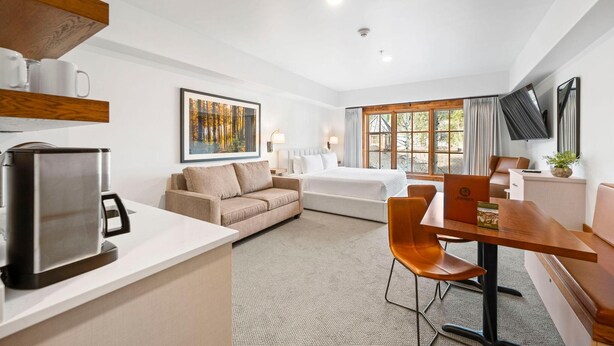 A hotel room with a bed, a sofa, a dining table, a coffee maker, and a TV. - Moonlit Oak | Includes Two 1-Day Lift Tickets (Tamarack)